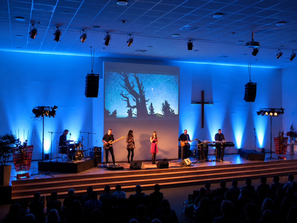 Live-Aufführung von Creation mit Musikern und Sängerinnen auf einer blau beleuchteten Bühne vor Publikum.